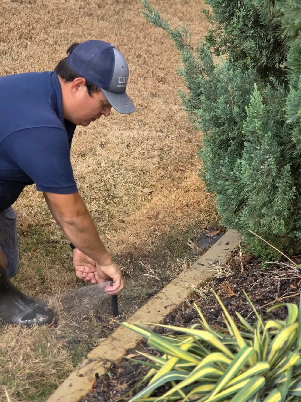 Technician adjusting irrigation head near landscape bed