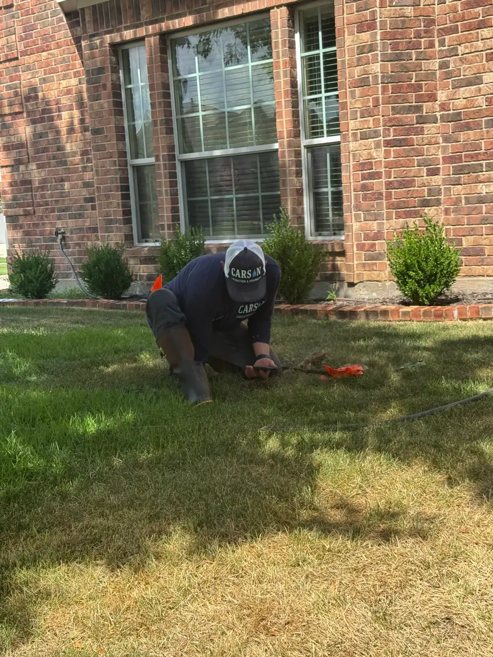 Carson tech repairing sprinkler line at brick home